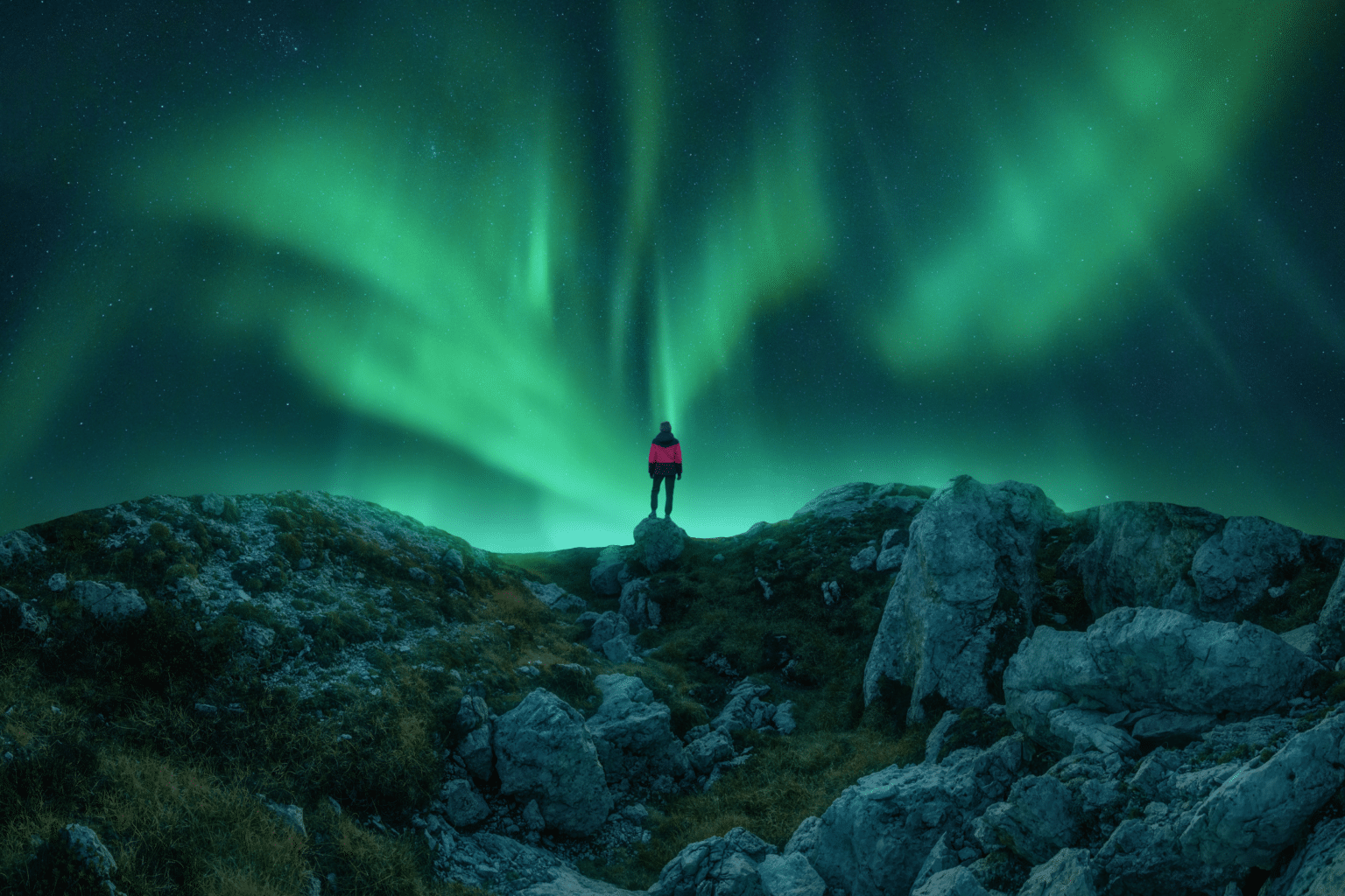 Un homme debout sur une colline sous une aurore boréale verte.