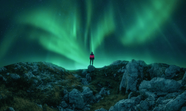 Een man staat op een heuvel onder groen noorderlicht.