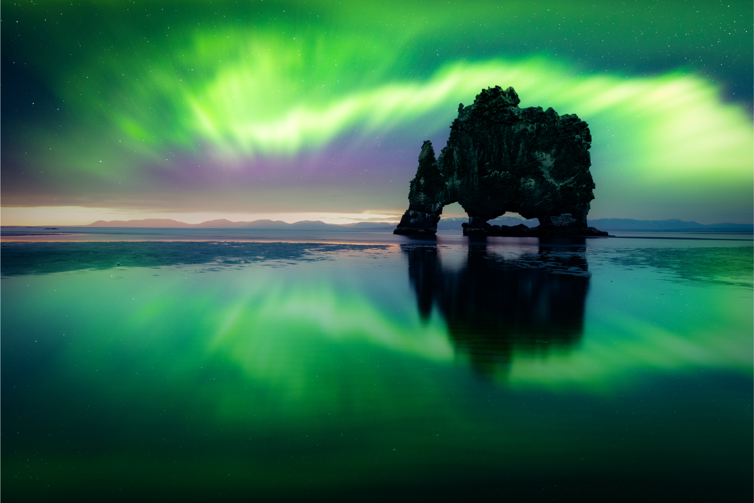 Green aurora reflected in a web black sand with Hvítserkur Rock standing tall, North Iceland.