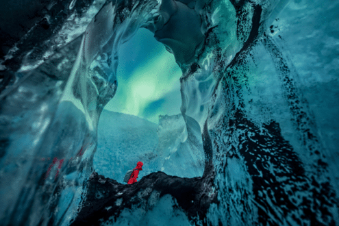 Prise de vue d'un homme et d'une aurore boréale depuis l'intérieur d'une grotte de glace.