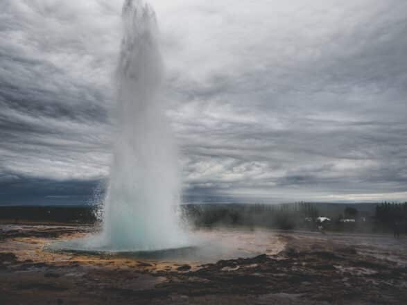 Le geyser Strokkur en éruption sur le Cercle d'Or avec un ciel gris en arrière-plan