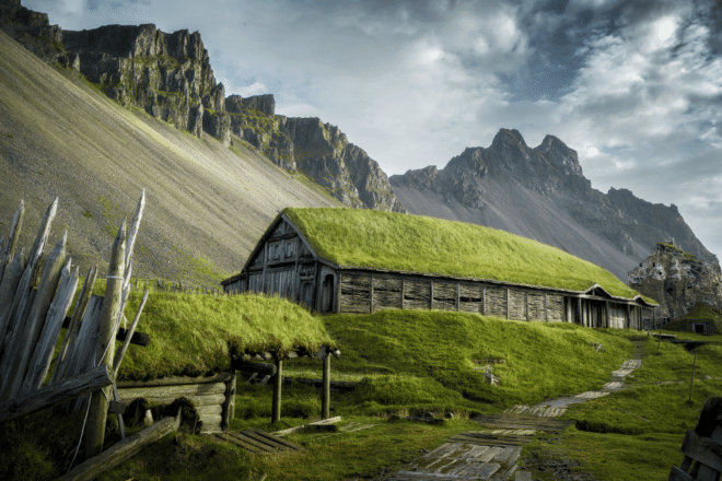 A wooden house with turf roof in front of a mountain in Iceland.