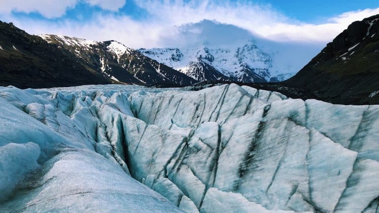 Glaciar blanco y azul en primer plano con montañas nevadas en la espalda en Islandia.