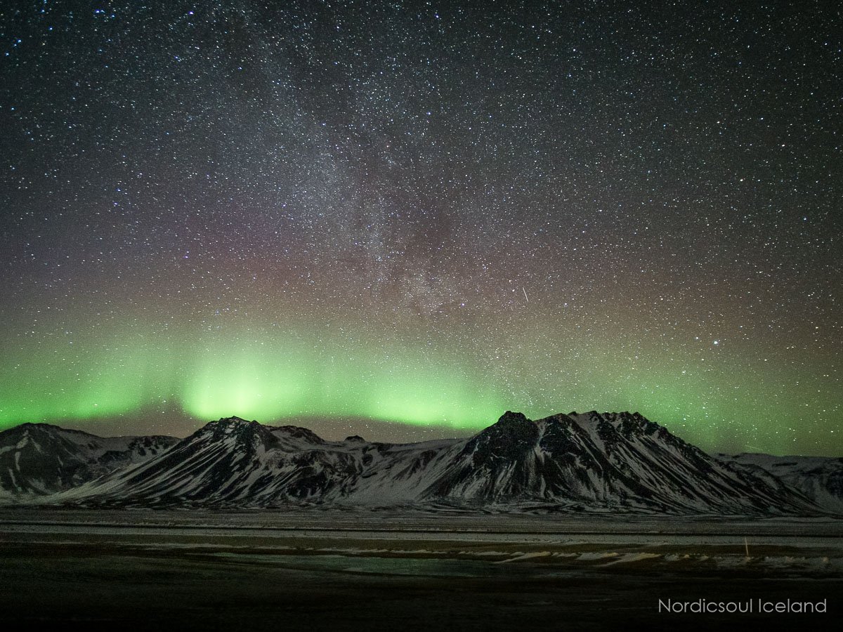 Aurora boreal sobre una montaña y bajo las estrellas