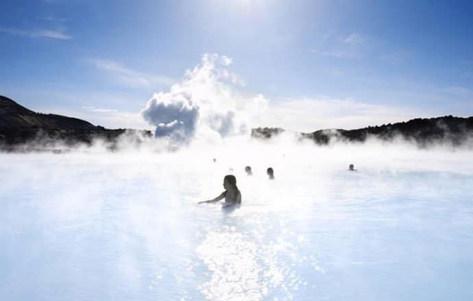 Mujeres en las sedosas aguas azules de la laguna azul en Islandia con humo en el fondo