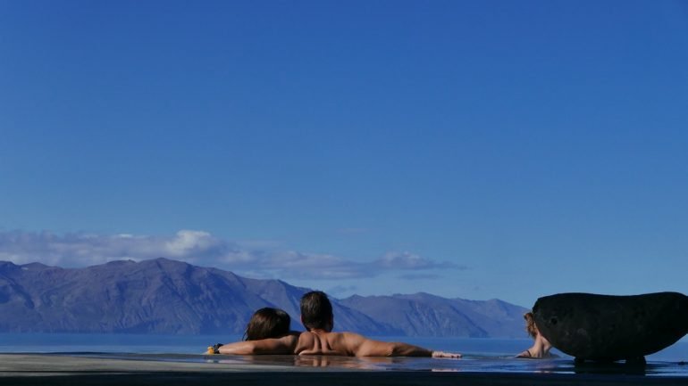 Dos personas bañándose en agua geotérmica mirando una montaña en Húsavík, Islandia