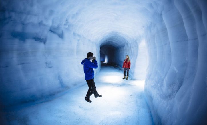 Ice tunnel inside the Langjökull glacier. A person in with a blue Jacket is taking a picture of a person in a red jacket inside the icy tunnel.