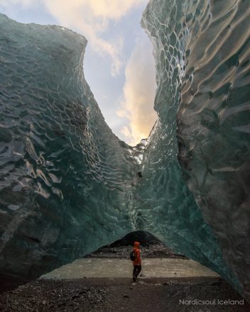 A person in front of a sheer block of ice at an ice cave in Vatnajökull National Park.