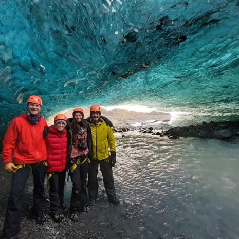 Un grupo de personas de pie frente a las paredes azules de una cueva de hielo en Islandia