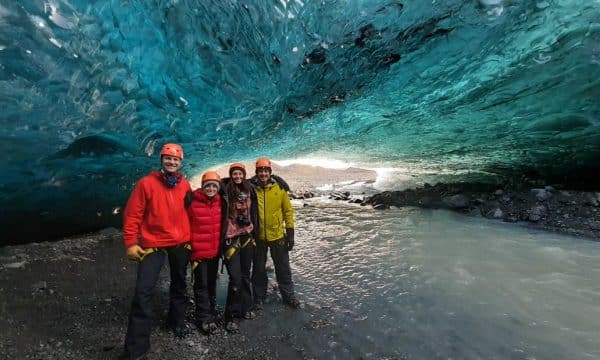 Un grupo de personas de pie frente a las paredes azules de una cueva de hielo en Islandia