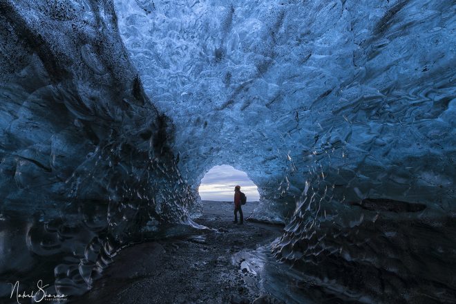 A person standing at the entry of a blue ice cave in Vatnajökull Glacier.