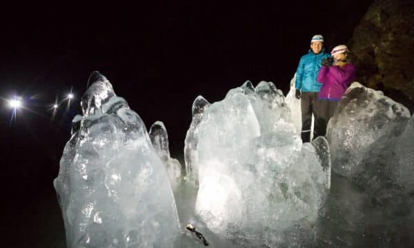 Two people in front of huge chunks of ice in Lofthellir Cave, North Iceland.