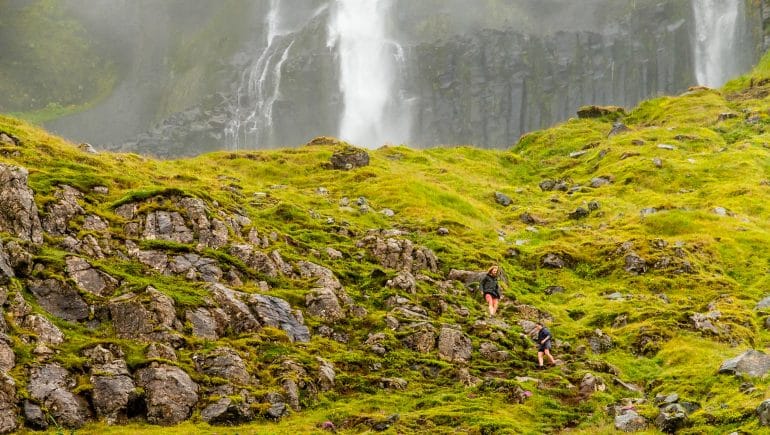 Two people hiking towards Bjarnafoss Waterfall on the Snaefellsnes Peninsula.