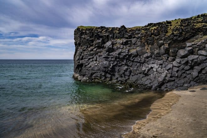 Une falaise menant à l'océan, entourée de sable doré sur la péninsule de Snaefellsnes.