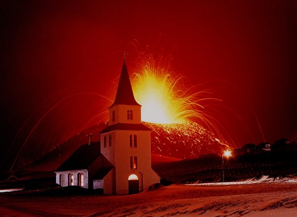 A volcano on the Westman Islands erupting behind a church.