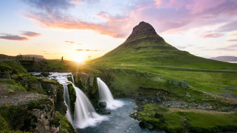 Mt. Kirkjufell and the nearby waterfall, sun shining behind the mountain.
