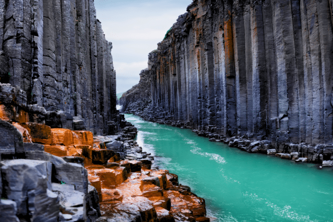 Een blauwgroene rivier stroomt tussen donkere basaltzuilrotsen in Studlagil Canyon, Oost-IJsland.