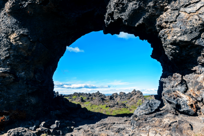 Una vista a través de una roca de lava de un campo de lava y un cielo azul en Dimmuborgir, Islandia.