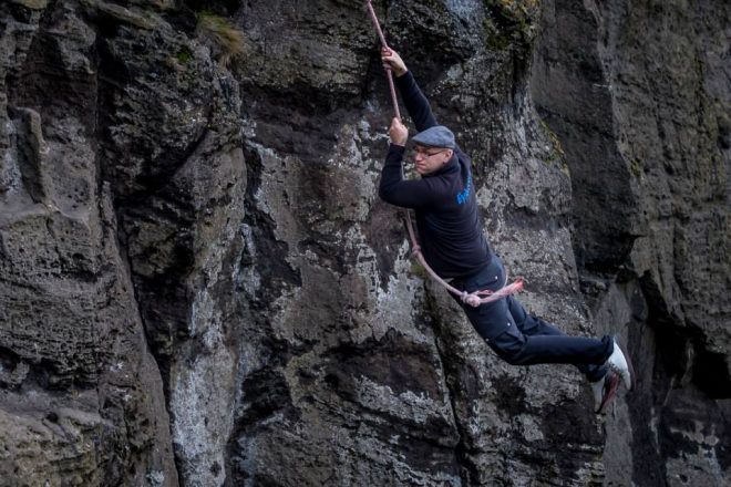 Un hombre sujetando una cuerda y balanceándose desde un acantilado en las Islas Westman.