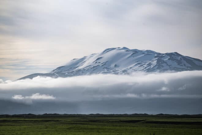 Snow-covered Hekla Volcano towering above clouds in South Iceland