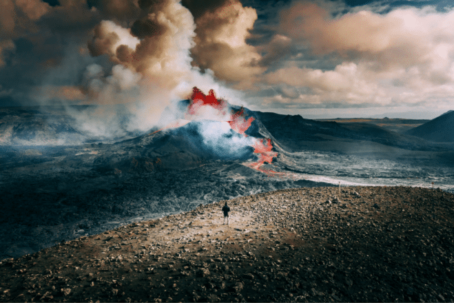 Un homme debout devant une éruption volcanique en Islande.