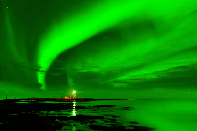 Green sky from northern lights reflected in a calm ocean at Grotta Lighthouse in Iceland.