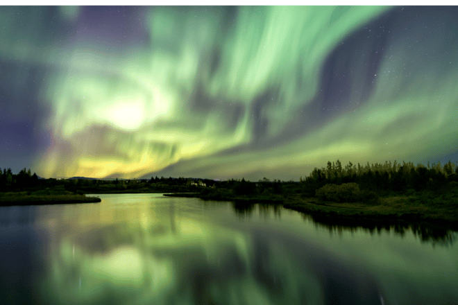 Green and purple northern lights in a sky above a lake in Iceland
