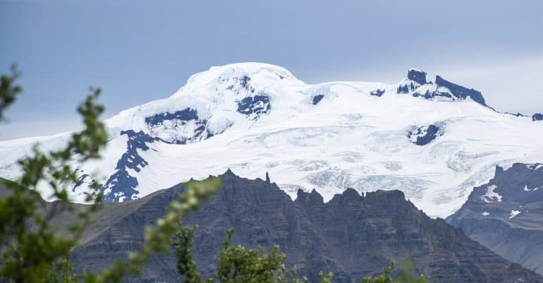 A snow-capped mountain towering over trees at Skaftafell Nature Reserve