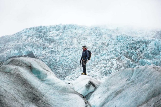 A man in glacier gear standing on a glacier, surrounded by ice