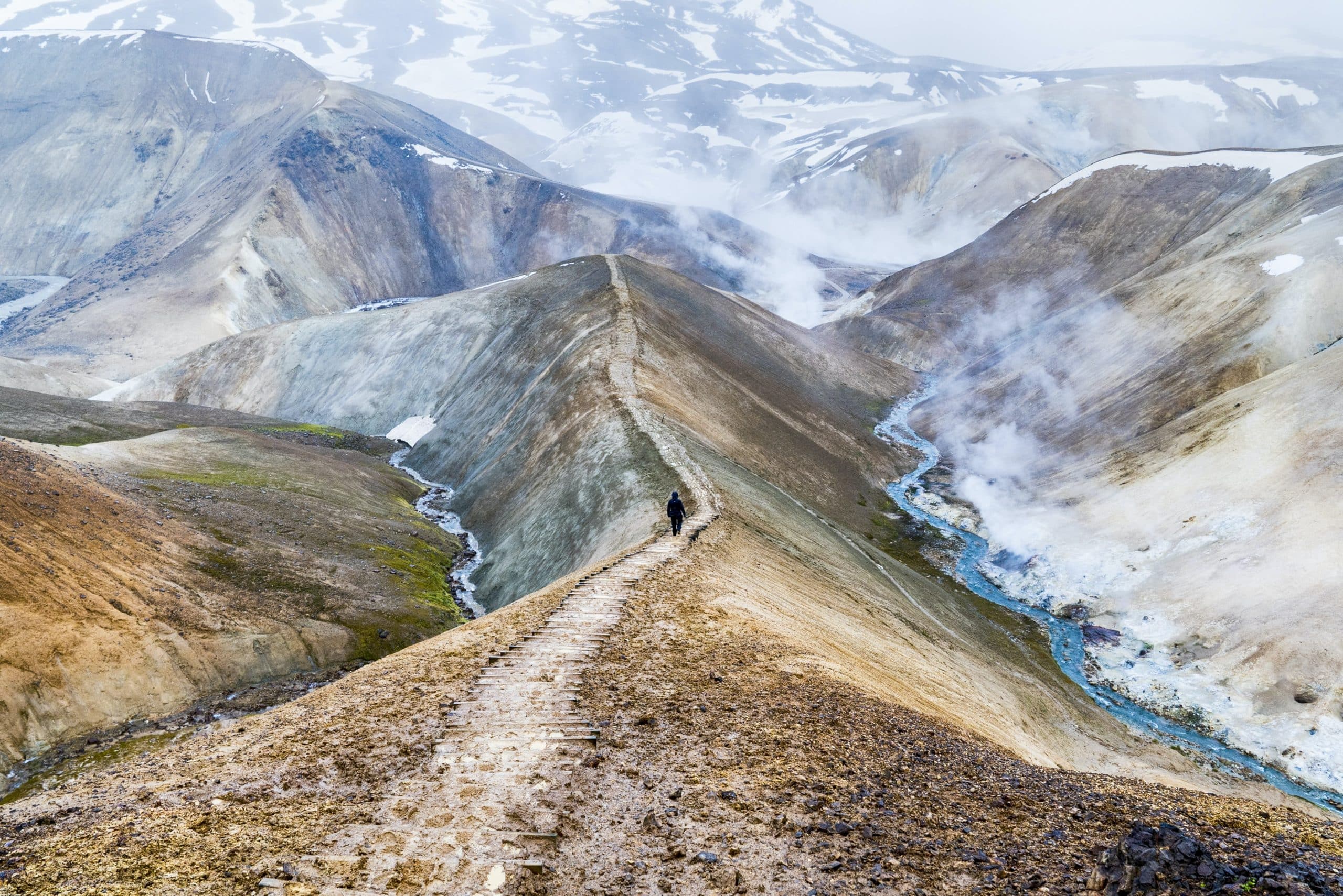 Una persona caminando por un sendero en las Tierras Altas de Islandia, rodeada de montañas humeantes.