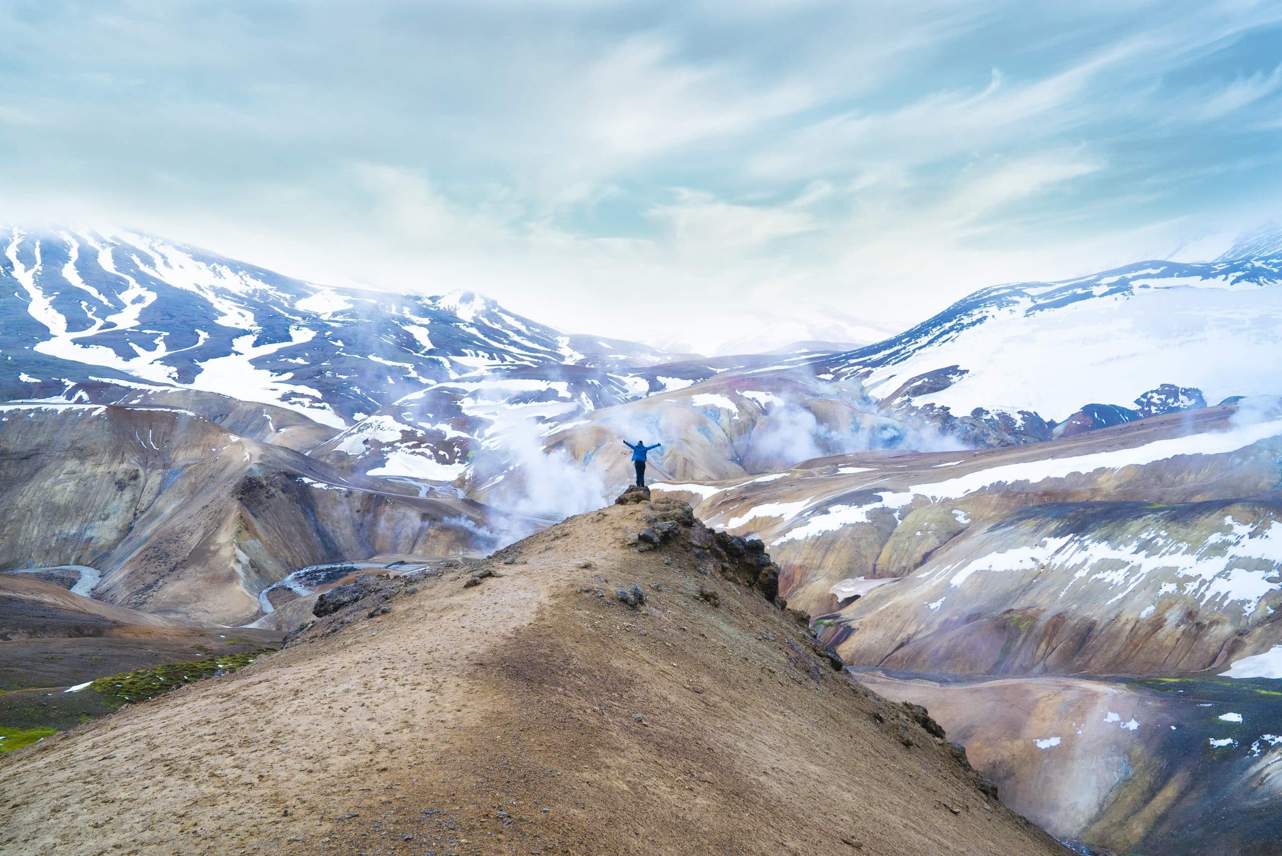 Una persona parada en un acantilado frente a una cadena montañosa en las Tierras Altas de Islandia.