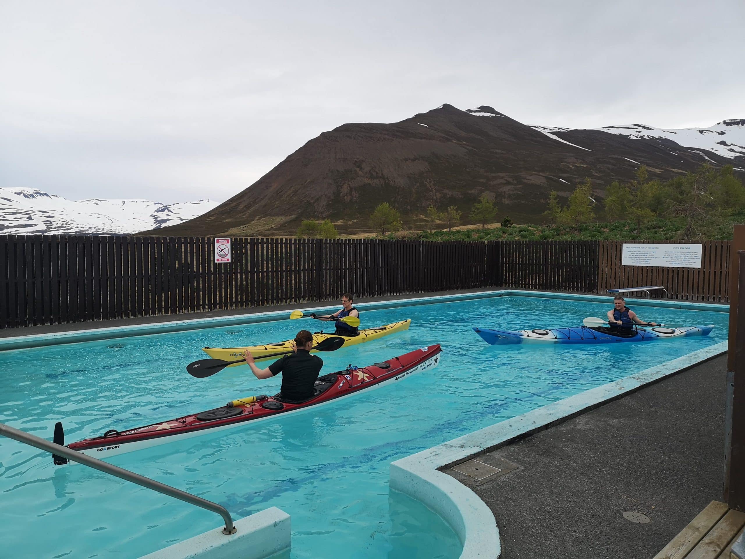 Trois personnes en kayak dans une piscine, les montagnes du nord de l'Islande en arrière-plan.