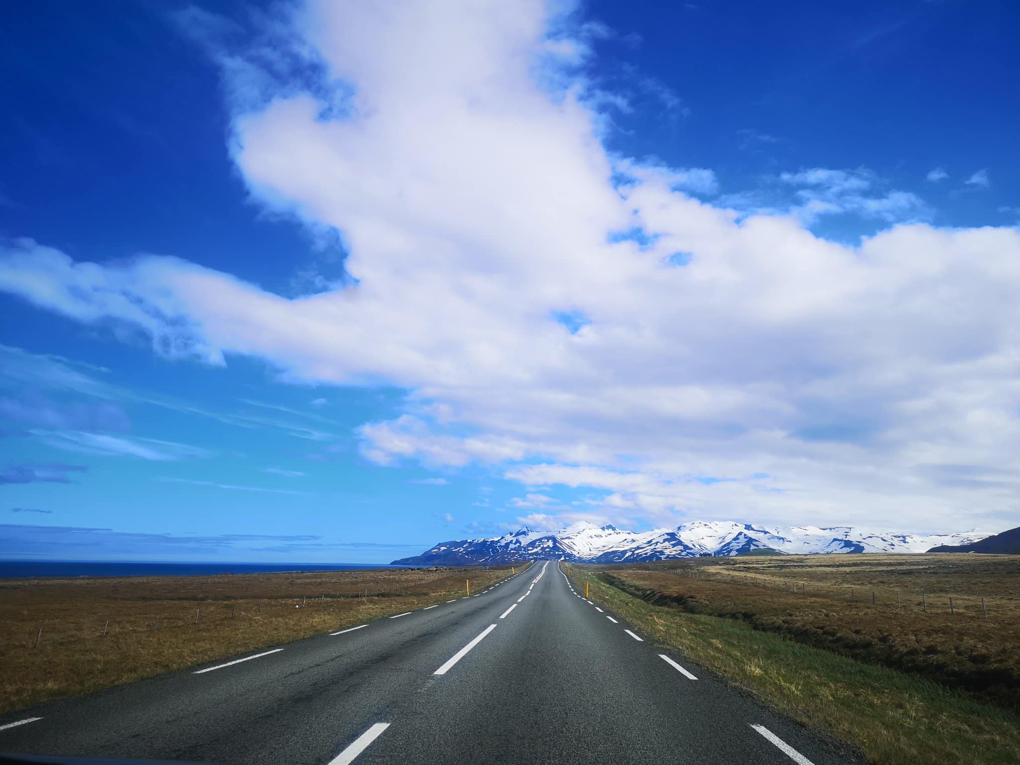 Carretera en el norte de Islandia con cielo azul y montañas a lo lejos.