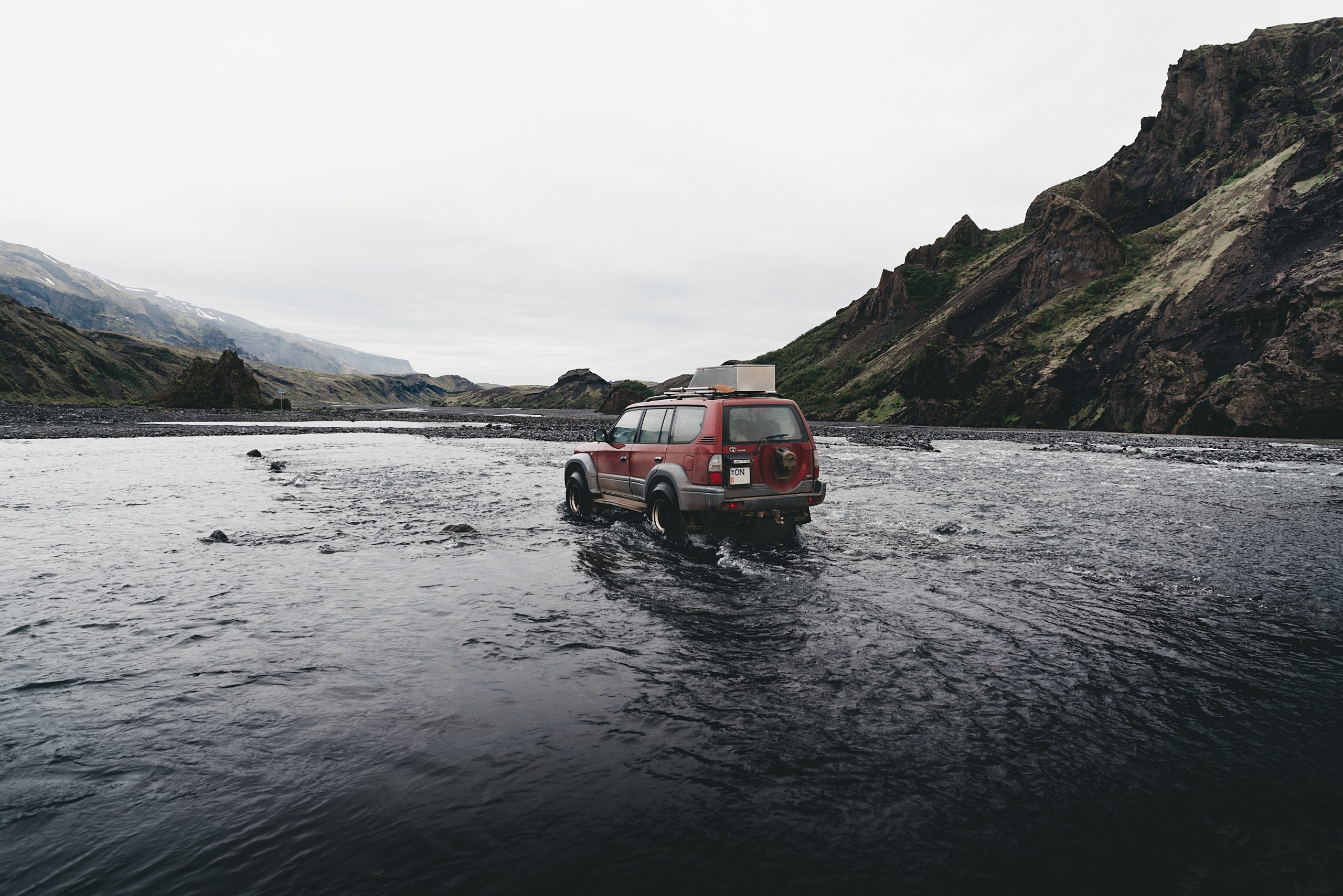 Un coche rojo cruzando un río en las Tierras Altas de Islandia.