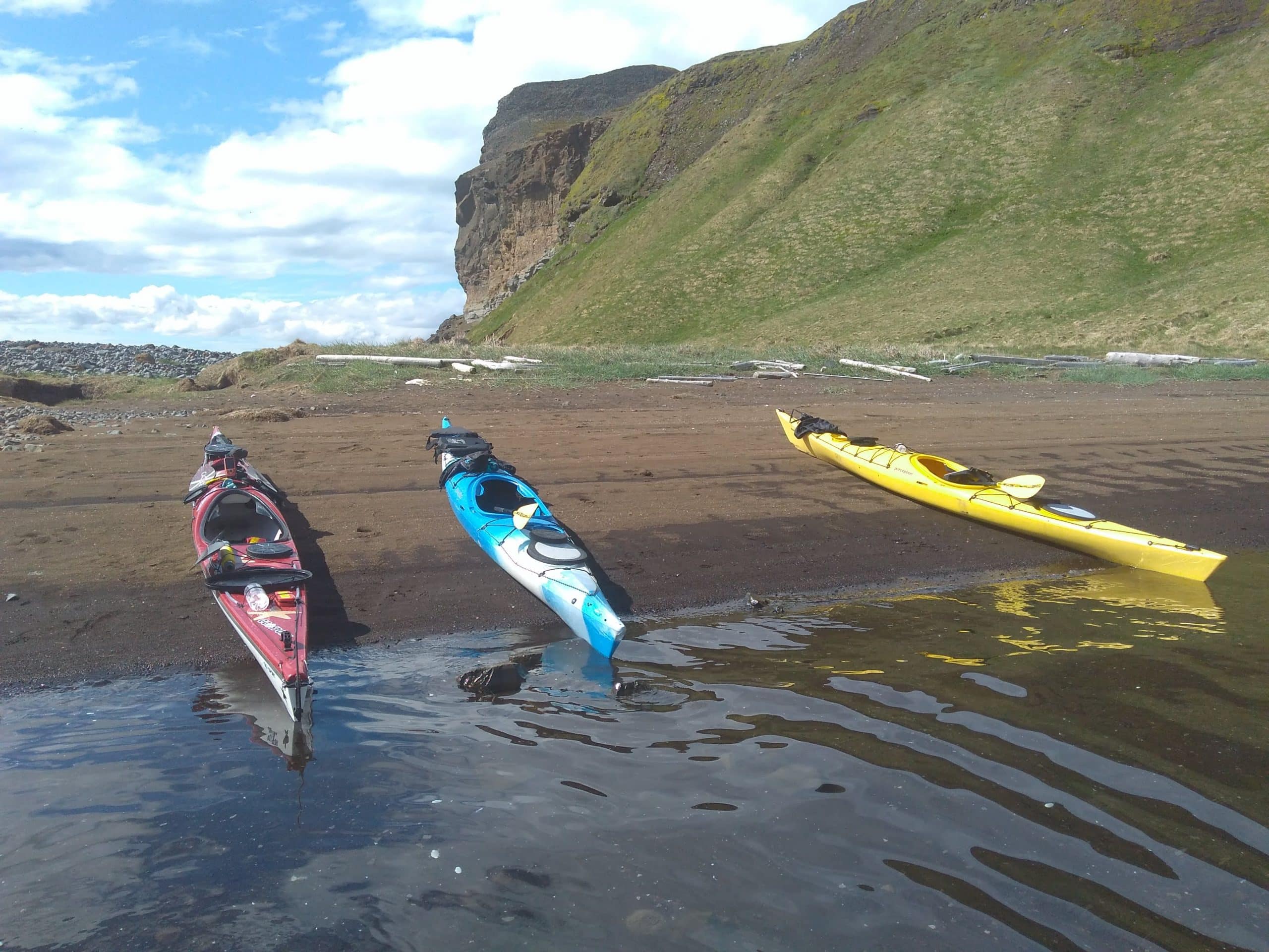Three kayaks on a beach in North Iceland, a green cliff in the background.