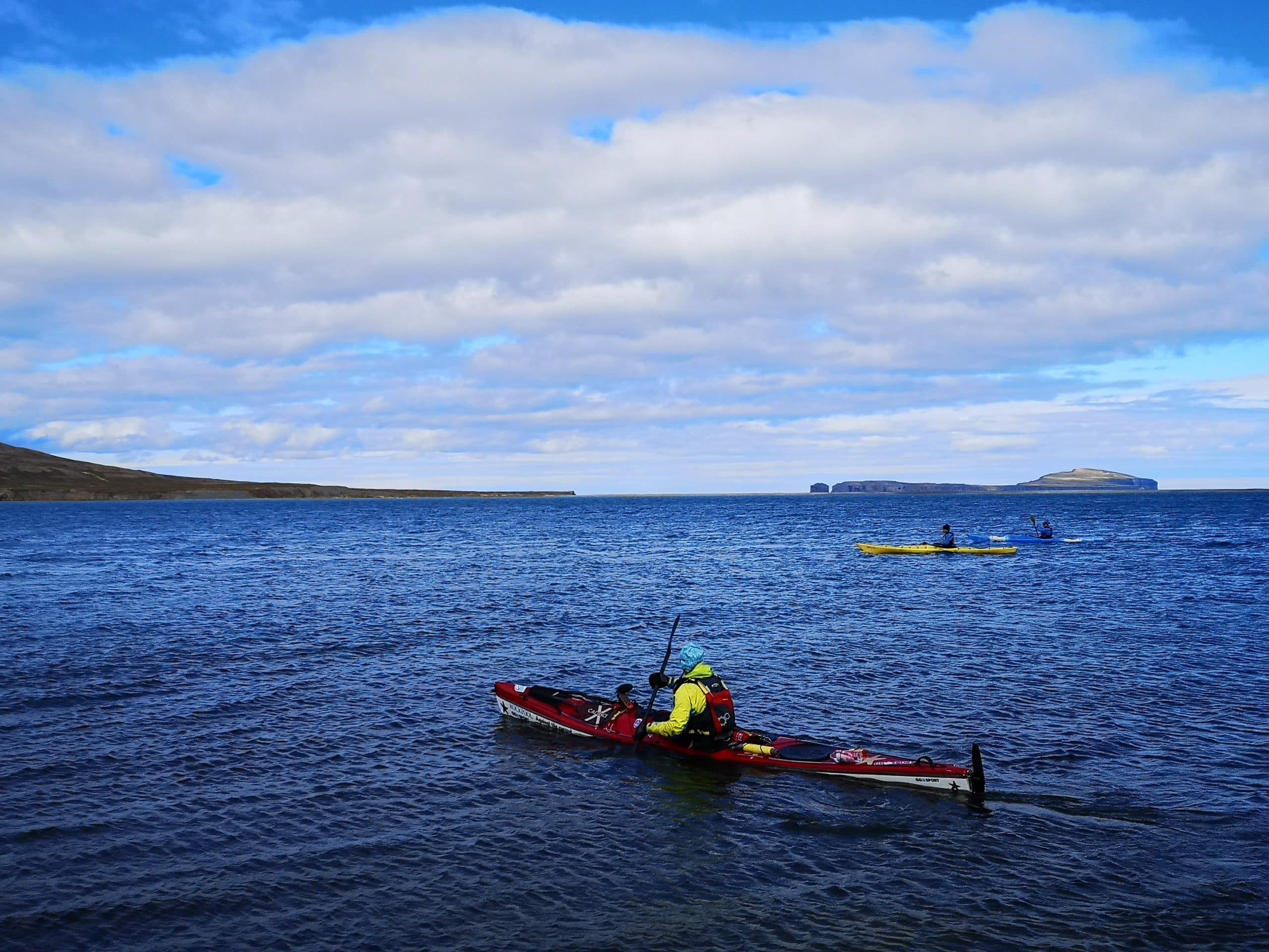 Tres kayakistas en aguas azules en el norte de Islandia.