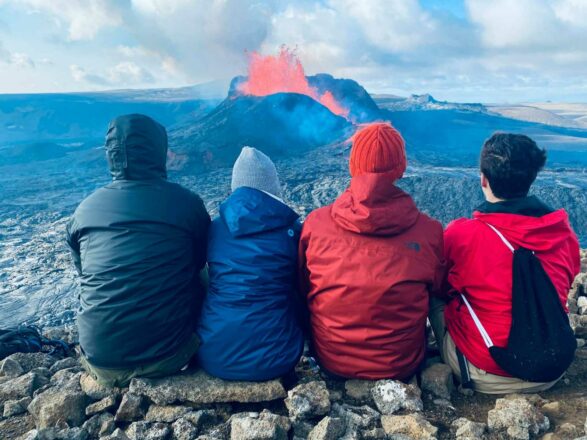4 people sitting and watching an erupting volcano in Iceland