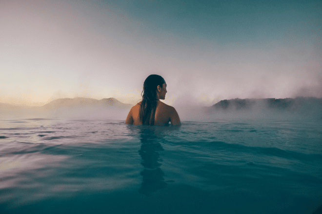 Una mujer desde atrás sumergiéndose en la Laguna Azul de Islandia, con poca luz y vapor saliendo del agua.