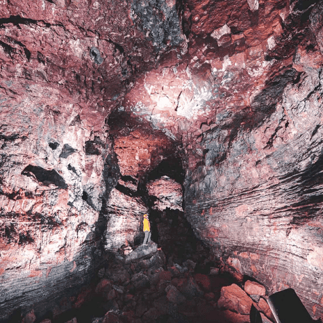 Une personne debout dans la grotte de Raufarhólshellir, en Islande, entourée de ses murs rouges.