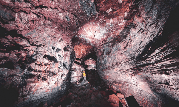 Una persona de pie en la cueva Raufarhólshellir, Islandia, rodeada por sus paredes rojas.