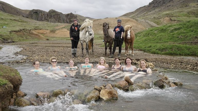 People in a hot spring with horses standing by.