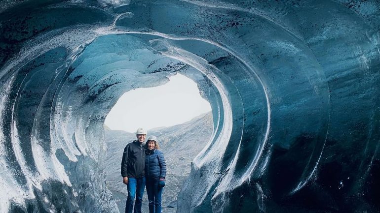 Dos personas de pie frente a la entrada de una cueva de hielo en Islandia