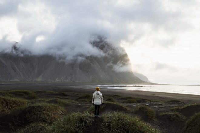 Voyageur seul debout sur du sable noir devant une montagne en Islande.
