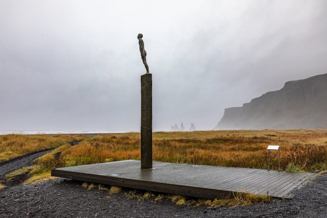 Estatua de un hombre en Vik, Islandia con montañas al fondo