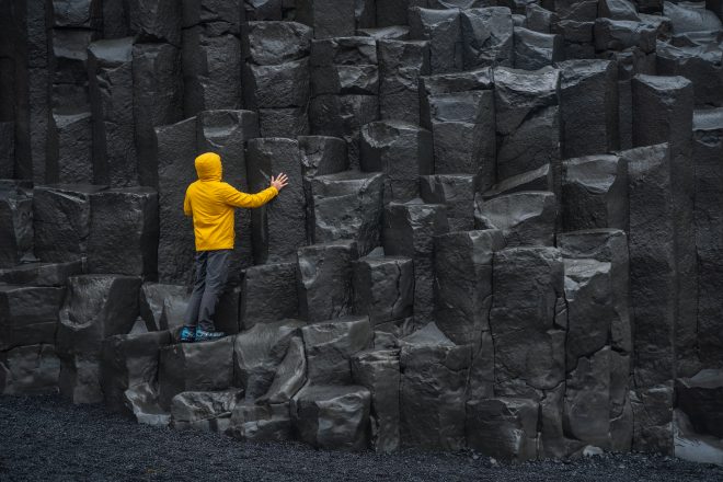 Hombre adulto con chaqueta amarilla de pie sobre columnas de basalto en Reynisfjara Black Sand Beach en Islandia