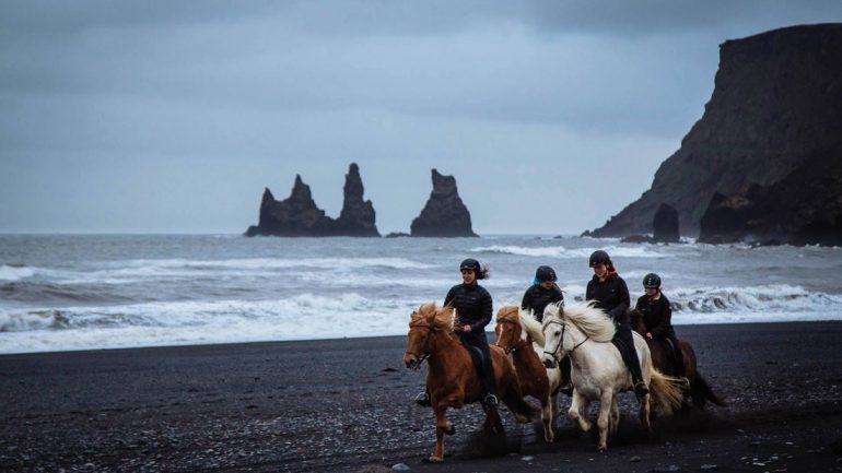 Les gens qui montent le cheval islandais sur une plage de sable noir près de Vík dans le sud de l'Islande