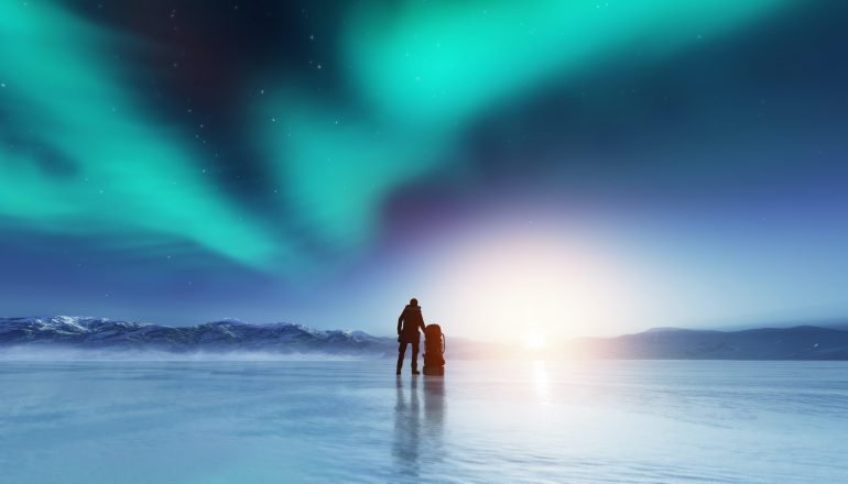 Hombre aventurero parado en un lago congelado con una mochila, mirando la aurora boreal.