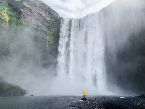 A man in a yellow raincoat in front of Skogafoss Waterfall in Iceland