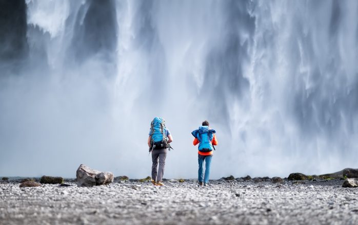 Un couple de voyageurs regarde la cascade de Skogafoss en Islande