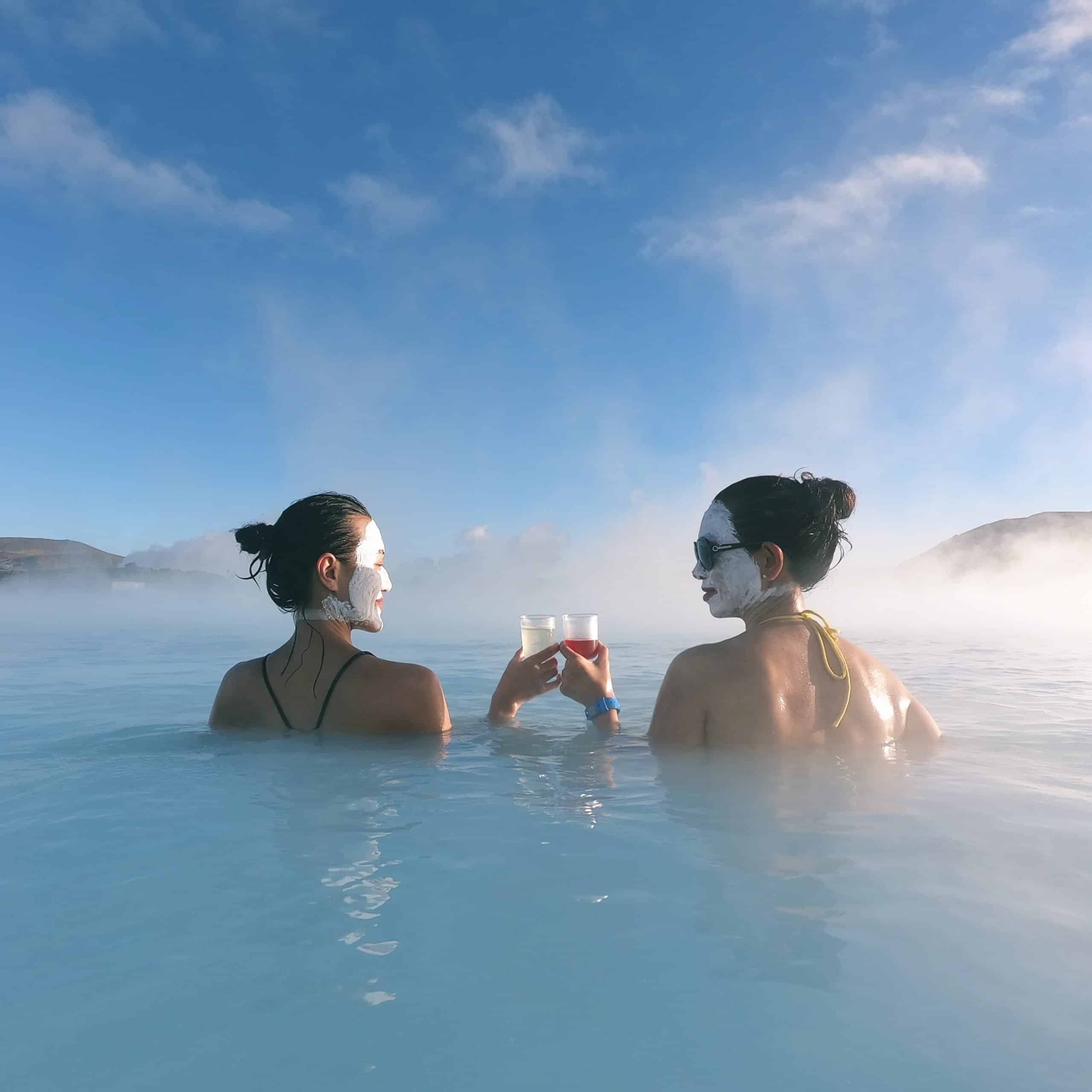 Dos mujeres con mascarillas de sílice disfrutando de una bebida en la Laguna Azul, Islandia